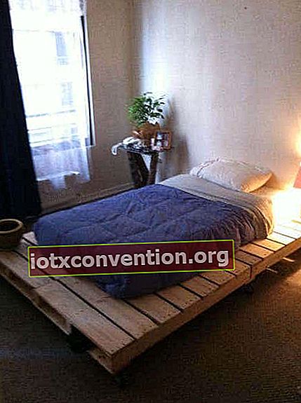 Tempat tidur dengan alas palet kayu mentah dan lampu samping tempat tidur