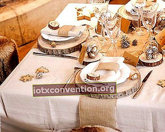 Kayu gelondongan sebagai meja diletakkan di atas taplak meja putih dengan piring, gelas, dan alat makan