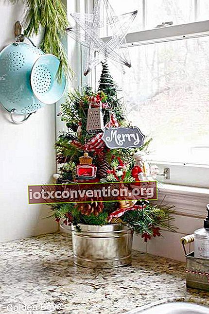 En liten julgran dekorerad och planterad i en kruka framför köksfönstret