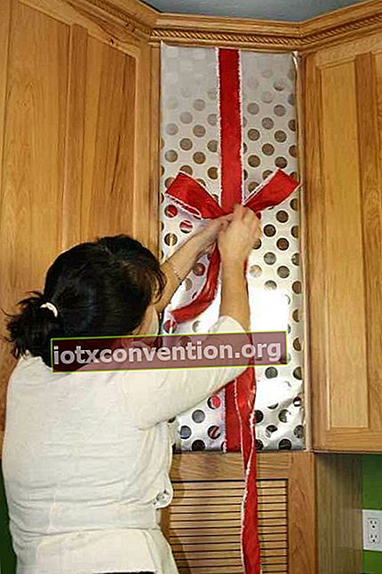 Frau, die ein rotes Band an einer Küchenschranktür als Weihnachtsdekoration hängt
