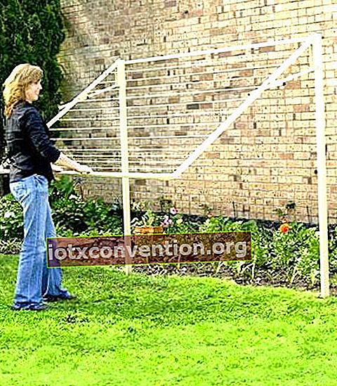 Seorang wanita menggunakan rak pengeringan yang boleh ditarik yang disimpan secara menegak di kebun.