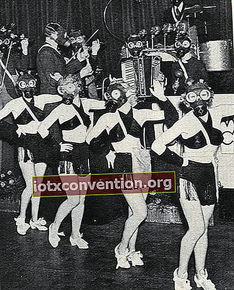 Flera kvinnor på en scen klädd i klädsel med en mask och musiker bakom sig