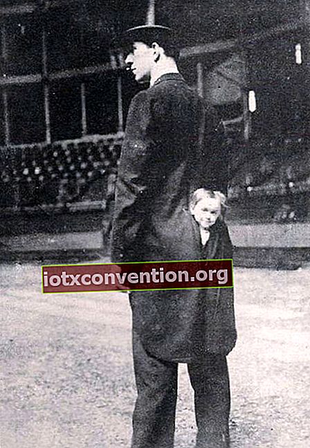 Mann mit einer langen schwarzen Jacke und einem kleinen Mädchen, das ihren Kopf aus dem Rücken der Jacke streckt