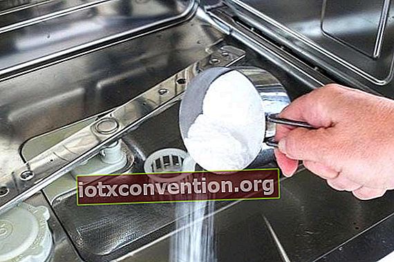 Una mano che versa il bicarbonato di sodio in una lavastoviglie vuota.