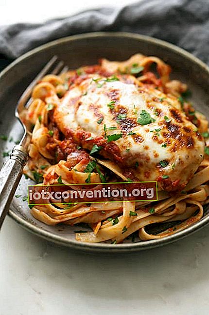 ayam dengan mozzarella dan tomat disajikan di atas piring dan dengan garpu dari jarak dekat