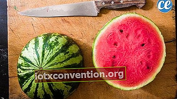 En lång kniv och en vattenmelon skuren i hälften på en träskiva.