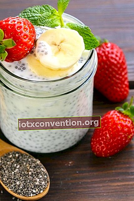 Masukkan biji chia ke balang yogurt dengan strawberi segar, di atas meja kayu.