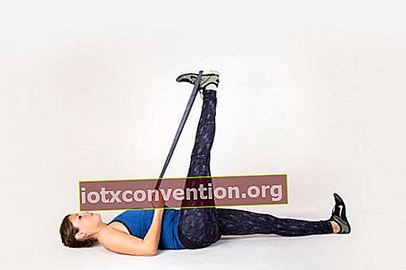 Frau zurück zum Boden mit erhobenem Bein und einem Gummiband, das gegen schmerzendes Knie hängt