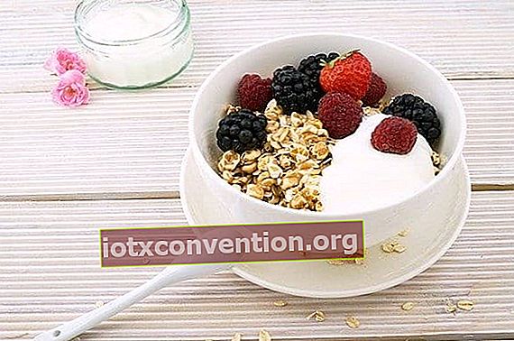 Eine weiße Schüssel Haferflocken mit Joghurt und hölzernen Erdbeeren und einem Löffel, der auf einem Holztisch liegt