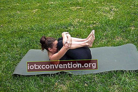 postur yoga pembebasan angin dengan wanita dalam celana ketat hitam di atas rumput