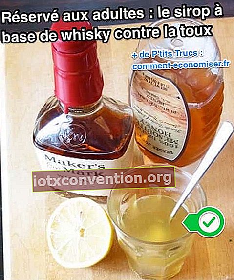 Una bottiglia di whisky e miele e mezzo limone vengono posti accanto a un bicchiere contenente il rimedio
